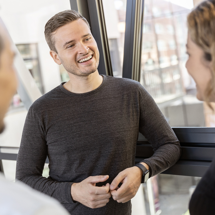 Mand i graa troeje taler med kollegaer